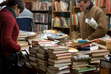 People browsing a table with stacks of piled books.